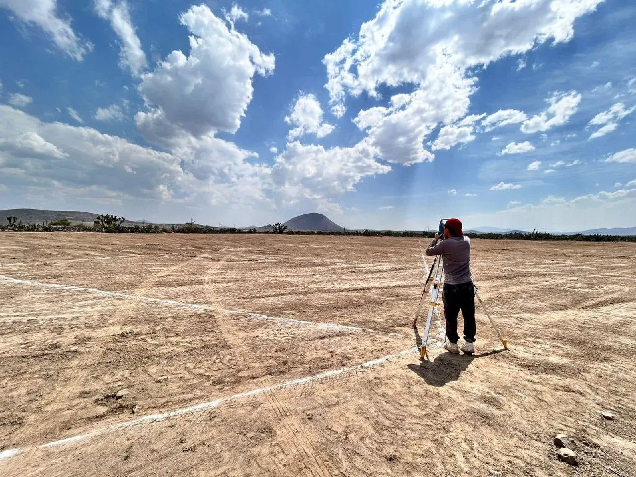 Topógrafo midiendo con estación total un terreno ya trazado con cal, con el cerro al fondo.